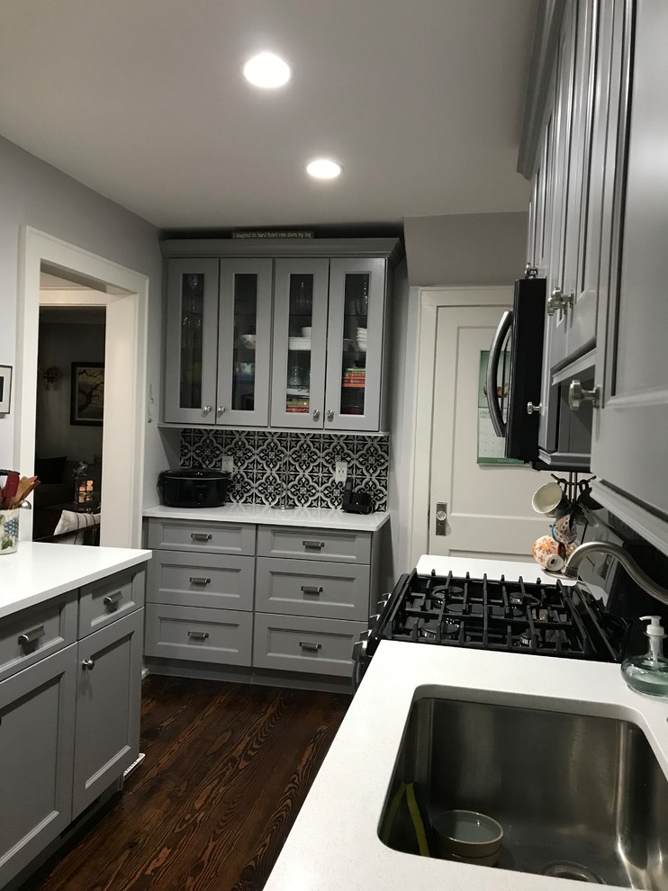 Small transitional galley medium tone wood floor and brown floor kitchen photo with an undermount sink, shaker cabinets, gray cabinets, quartz countertops, multicolored backsplash, porcelain backsplash, black appliances and no island
