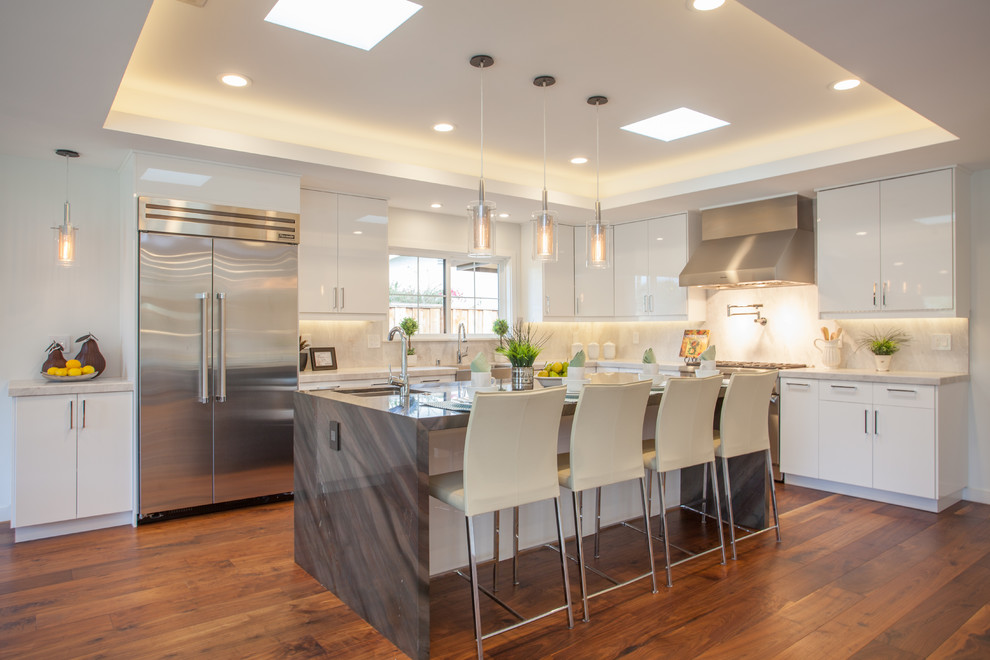 Kitchen - large transitional l-shaped medium tone wood floor kitchen idea in Dallas with a farmhouse sink, flat-panel cabinets, white cabinets, white backsplash, stone slab backsplash, stainless steel appliances and an island