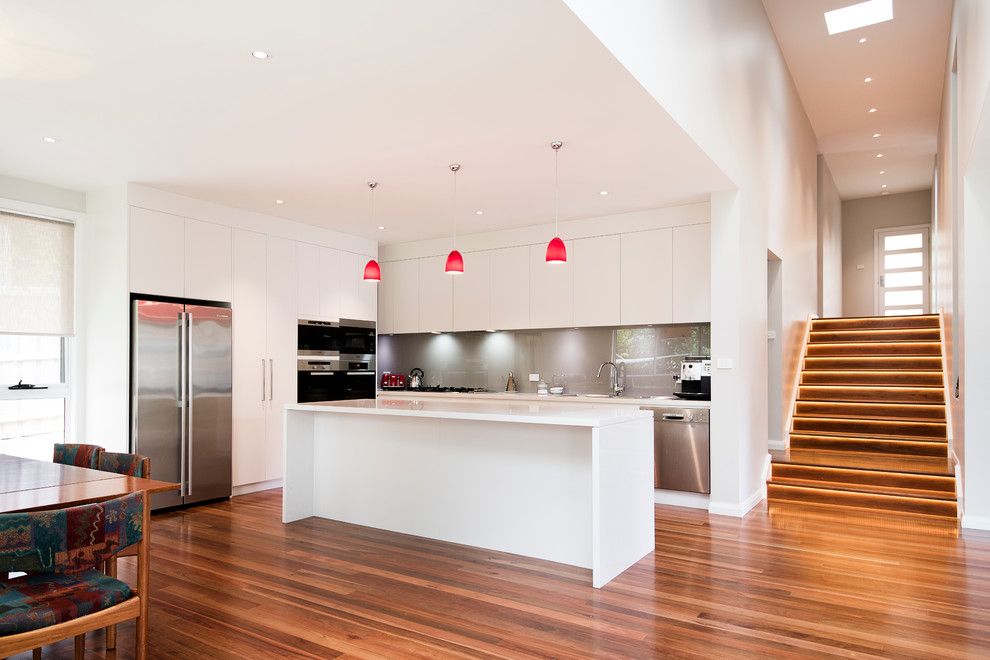 Inspiration for a large contemporary l-shaped kitchen pantry in Sydney with flat-panel cabinets, white cabinets, with island, an undermount sink, grey splashback, glass sheet splashback, stainless steel appliances and medium hardwood floors.