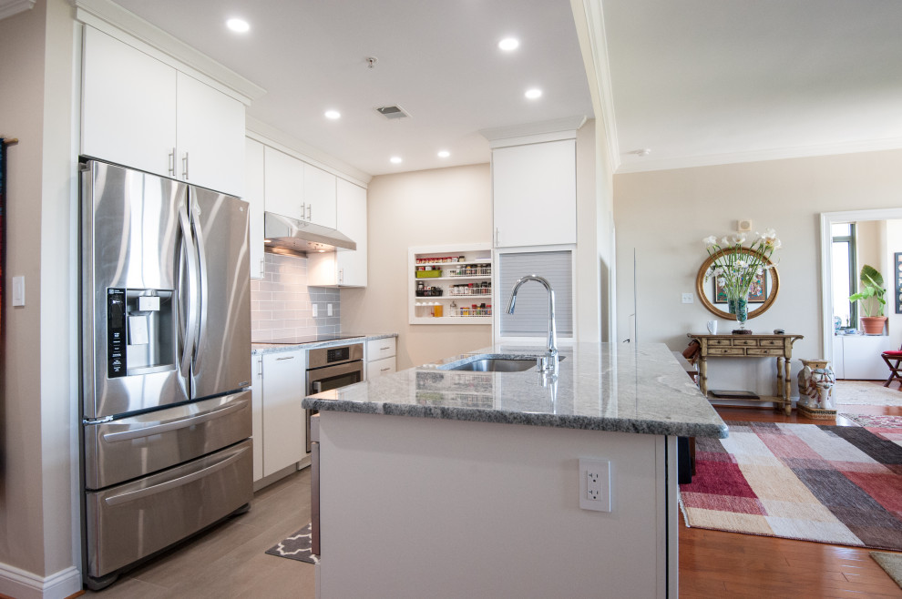 Photo of a small contemporary galley kitchen in DC Metro with an undermount sink, flat-panel cabinets, white cabinets, granite benchtops, grey splashback, porcelain splashback, stainless steel appliances, porcelain floors, a peninsula, grey floor and grey benchtop.