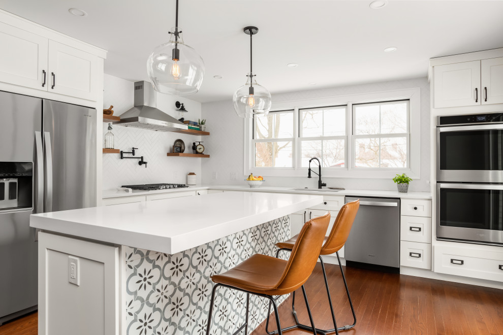 Transitional medium tone wood floor and brown floor kitchen photo in Philadelphia with an undermount sink, shaker cabinets, white cabinets, white backsplash, ceramic backsplash, stainless steel appliances, an island and white countertops