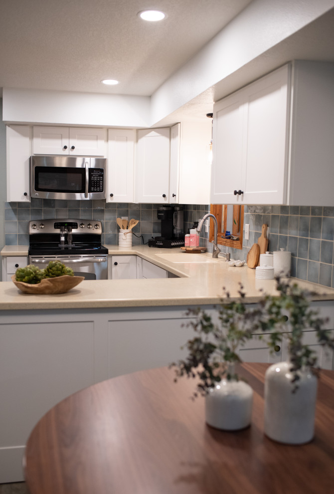 Example of a mid-sized transitional u-shaped slate floor and multicolored floor enclosed kitchen design with an integrated sink, shaker cabinets, white cabinets, solid surface countertops, blue backsplash, ceramic backsplash, stainless steel appliances and beige countertops