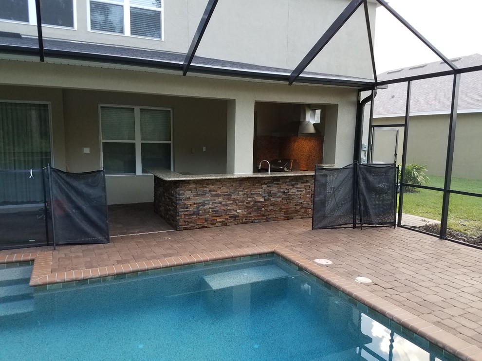 Large country backyard patio in Tampa with an outdoor kitchen, concrete pavers and a roof extension.