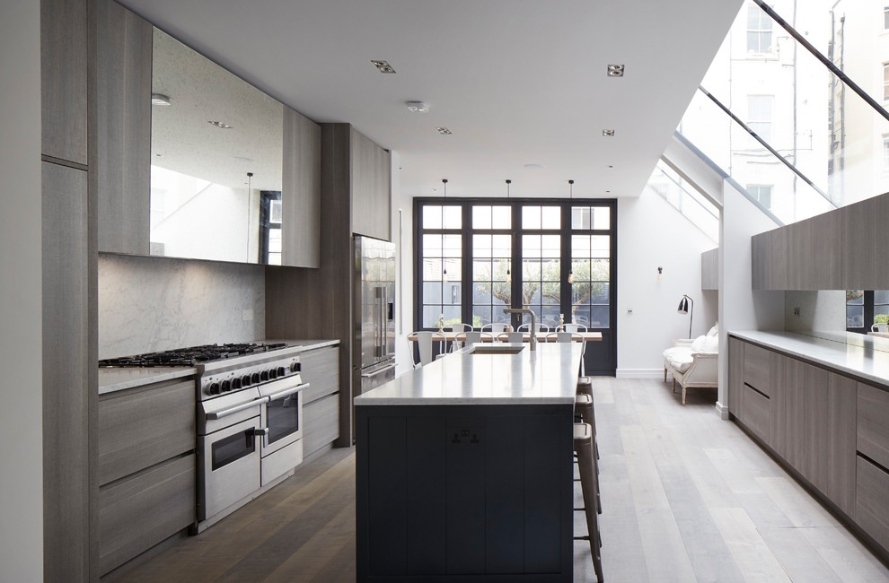 This is an example of a contemporary galley kitchen in London with an undermount sink, flat-panel cabinets, beige splashback, stainless steel appliances, light hardwood floors, with island and brown floor.