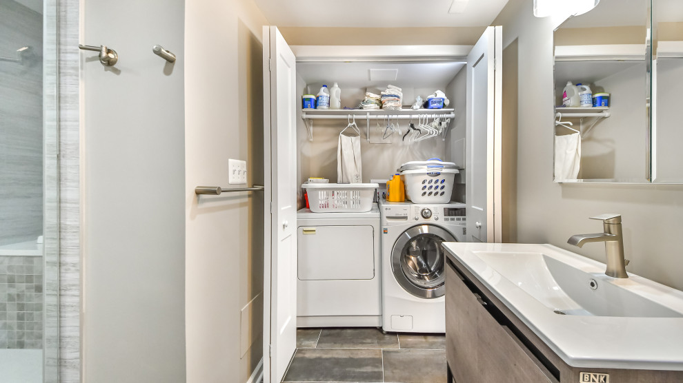 Foto på en liten vintage liten tvättstuga, med vita väggar, klinkergolv i porslin, en tvättmaskin och torktumlare bredvid varandra och brunt golv