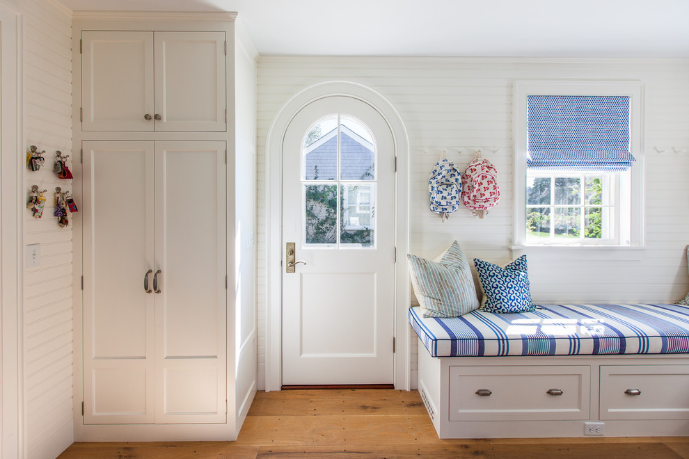 This is an example of a large beach style mudroom in Boston with white walls, medium hardwood floors, a single front door and a white front door.