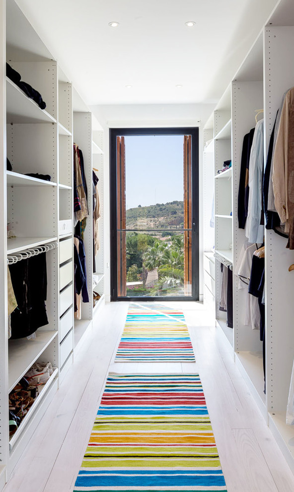 Mid-sized modern gender-neutral walk-in wardrobe in Barcelona with open cabinets, white cabinets and light hardwood floors.