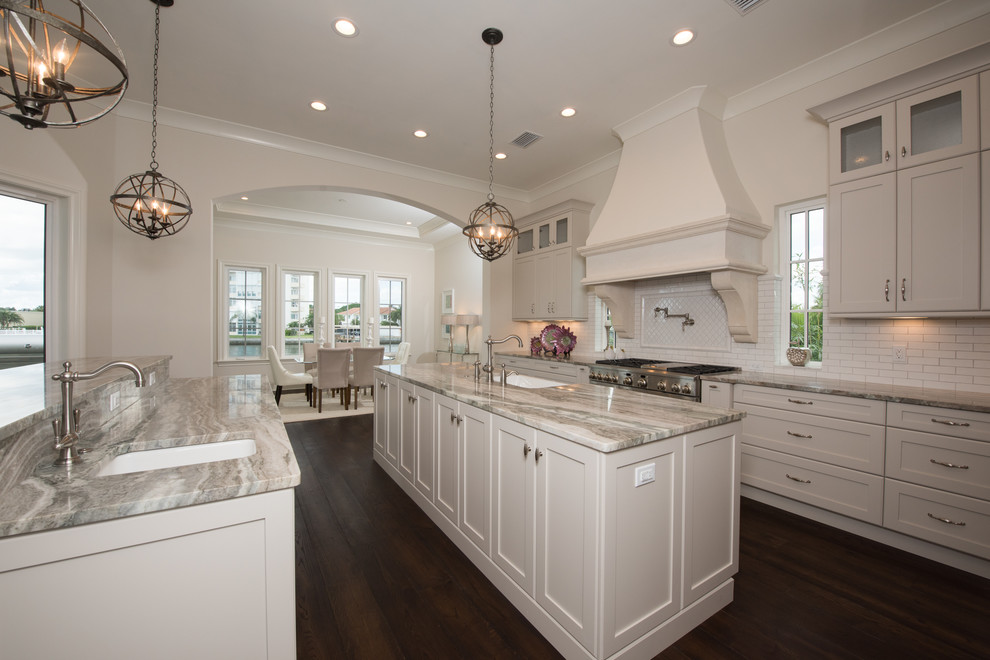 Photo of a large transitional galley eat-in kitchen in Tampa with a farmhouse sink, shaker cabinets, white cabinets, granite benchtops, white splashback, subway tile splashback, stainless steel appliances, dark hardwood floors and with island.