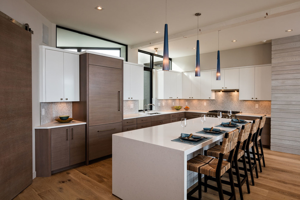 This is an example of a contemporary l-shaped kitchen in Milwaukee with an undermount sink, flat-panel cabinets, white cabinets, mosaic tile splashback, panelled appliances, light hardwood floors and with island.