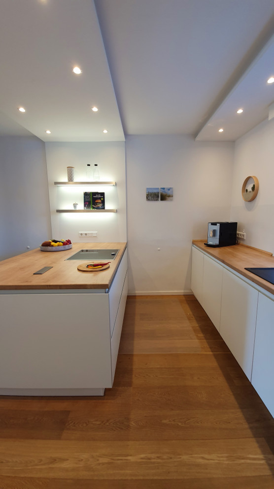Design ideas for a mid-sized traditional galley open plan kitchen in Dusseldorf with an integrated sink, flat-panel cabinets, white cabinets, wood benchtops, white splashback, window splashback, panelled appliances, dark hardwood floors, a peninsula, brown floor and brown benchtop.