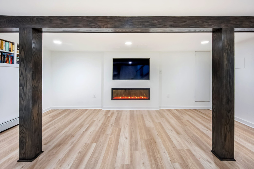 Aménagement d'un sous-sol classique donnant sur l'extérieur et de taille moyenne avec un mur blanc, un sol en vinyl, cheminée suspendue, un sol beige et poutres apparentes.