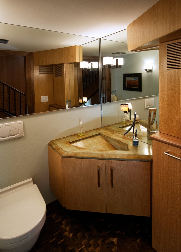 Photo of a mid-sized modern powder room in Philadelphia with flat-panel cabinets, light wood cabinets, a wall-mount toilet, grey walls, an integrated sink, onyx benchtops, brown floor and dark hardwood floors.