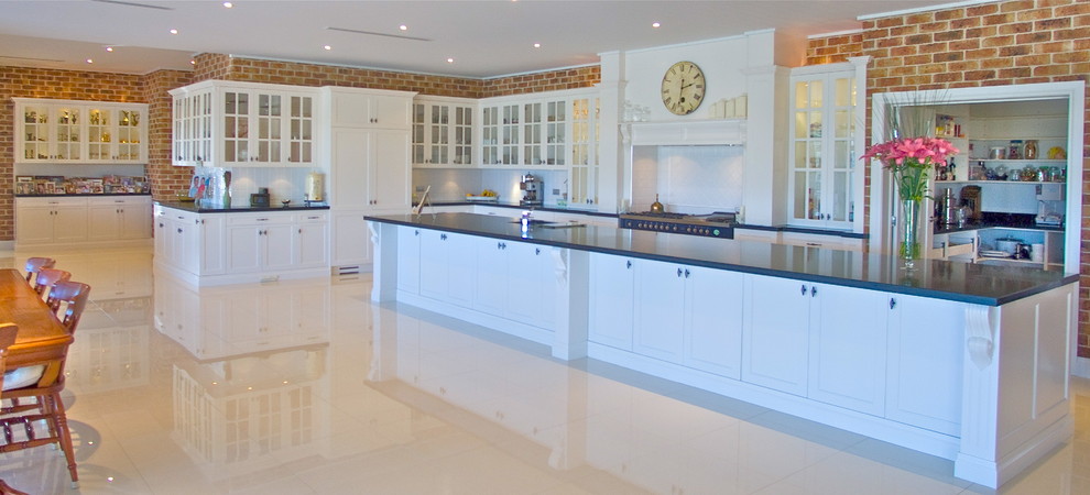 Photo of an expansive traditional l-shaped open plan kitchen in Sydney with an undermount sink, shaker cabinets, white cabinets, quartz benchtops, white splashback, ceramic splashback, black appliances, porcelain floors and with island.