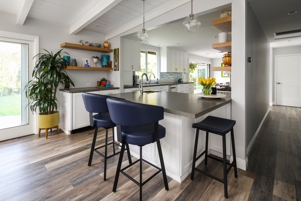 Inspiration for a mid-sized midcentury eat-in kitchen in San Diego with shaker cabinets, white cabinets, white splashback, ceramic splashback, stainless steel appliances, medium hardwood floors, a peninsula, grey floor and grey benchtop.