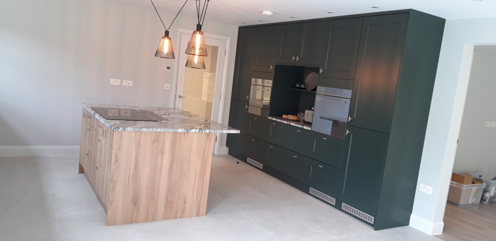 Contemporary open plan kitchen in Dorset with green cabinets, quartzite benchtops, stainless steel appliances, with island and multi-coloured benchtop.