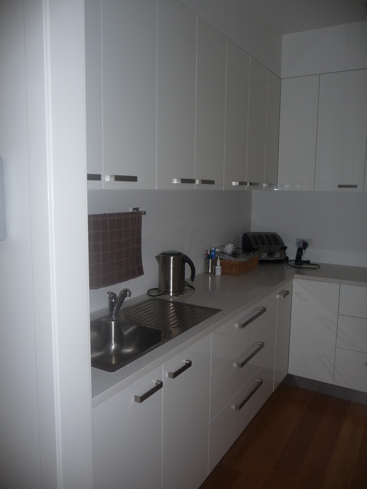 Photo of a large modern single-wall kitchen pantry in Brisbane with flat-panel cabinets, white cabinets, quartz benchtops, stainless steel appliances, light hardwood floors, with island and a double-bowl sink.