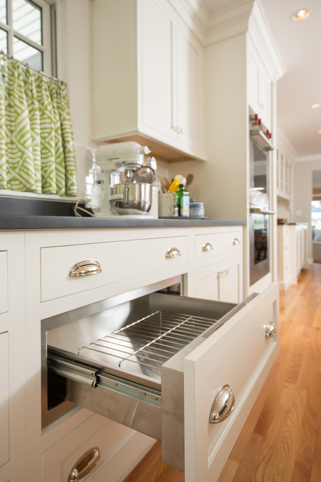 Kitchen - transitional medium tone wood floor kitchen idea in Boston with a farmhouse sink, recessed-panel cabinets, white cabinets, granite countertops, white backsplash, subway tile backsplash, stainless steel appliances and two islands