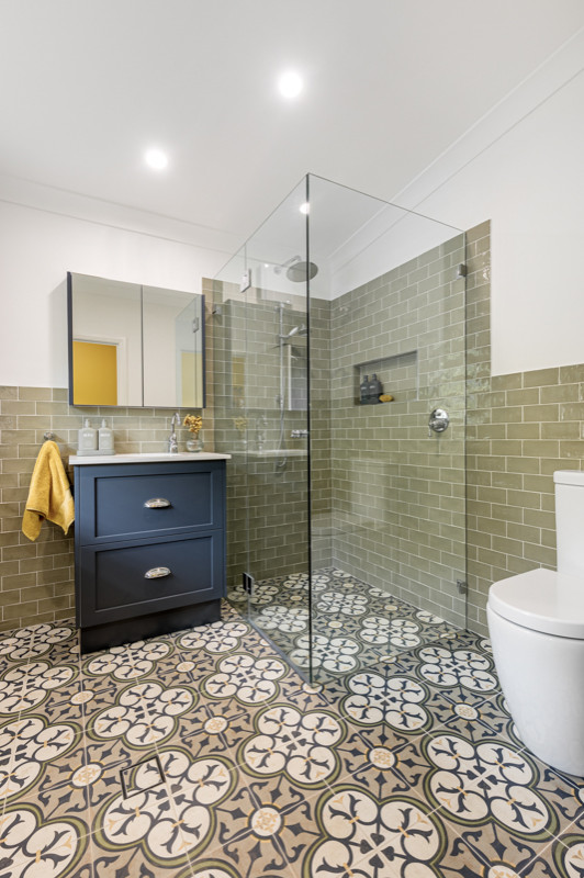 Mid-sized master bathroom in Sydney with shaker cabinets, blue cabinets, a corner shower, a two-piece toilet, green tile, white walls, an undermount sink, multi-coloured floor, a hinged shower door, white benchtops, a laundry, a single vanity and a freestanding vanity.