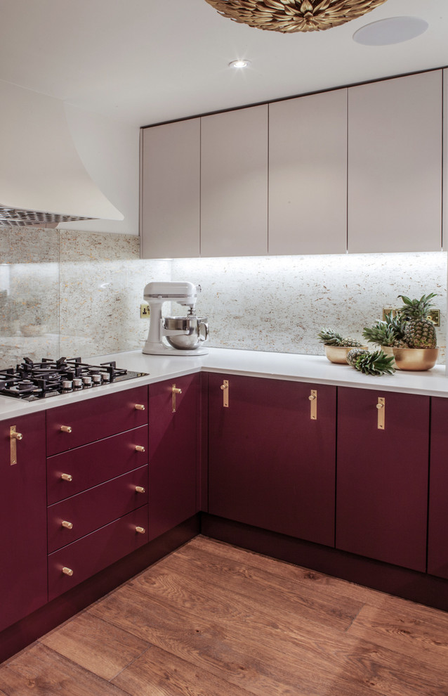 Photo of a contemporary u-shaped separate kitchen in London with a drop-in sink, flat-panel cabinets, red cabinets, solid surface benchtops, metallic splashback, stainless steel appliances, medium hardwood floors, no island and brown floor.