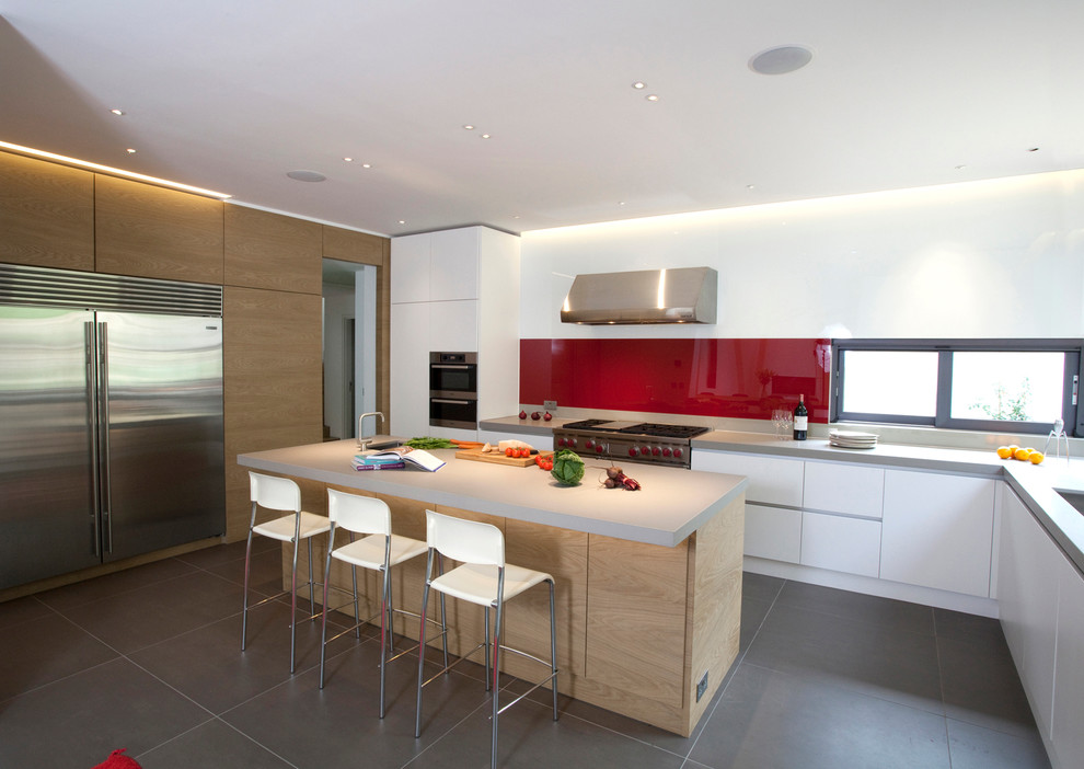 Large contemporary l-shaped open plan kitchen in Hertfordshire with a peninsula, flat-panel cabinets, medium wood cabinets, quartzite benchtops, red splashback, glass sheet splashback, stainless steel appliances, an undermount sink and ceramic floors.