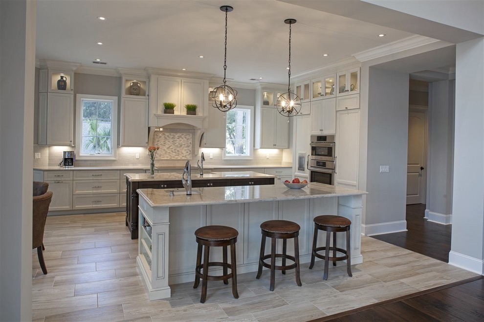 This is an example of a large traditional l-shaped eat-in kitchen in Atlanta with multiple islands, recessed-panel cabinets, white cabinets, granite benchtops, white splashback, subway tile splashback, stainless steel appliances, an undermount sink and porcelain floors.