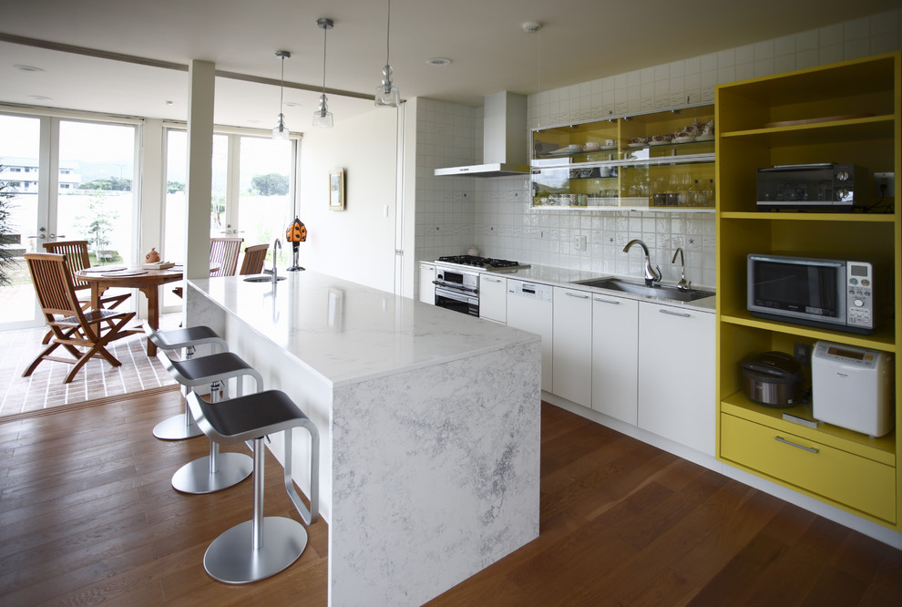 Inspiration for a modern single-wall open plan kitchen in Other with a single-bowl sink, flat-panel cabinets, white cabinets, marble benchtops, white splashback, ceramic splashback, medium hardwood floors, with island and brown floor.