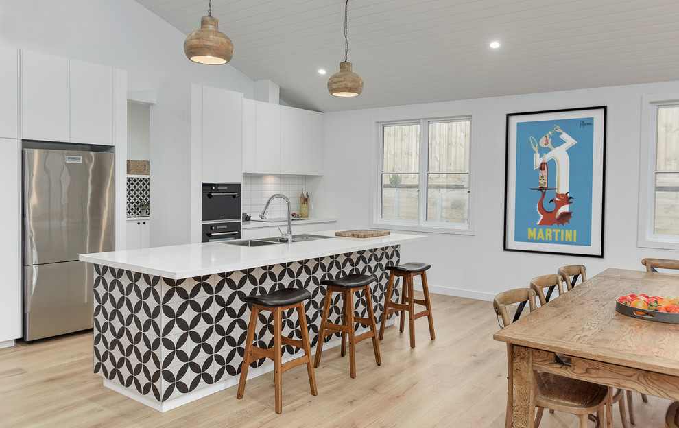Inspiration for a large contemporary single-wall eat-in kitchen in Melbourne with a farmhouse sink, flat-panel cabinets, white cabinets, quartz benchtops, white splashback, ceramic splashback, black appliances, light hardwood floors and with island.