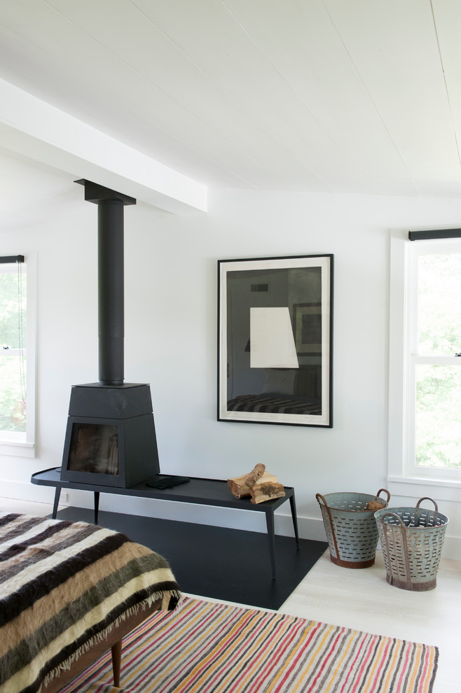 Mid-sized midcentury master bedroom in New York with white walls, painted wood floors and a wood stove.