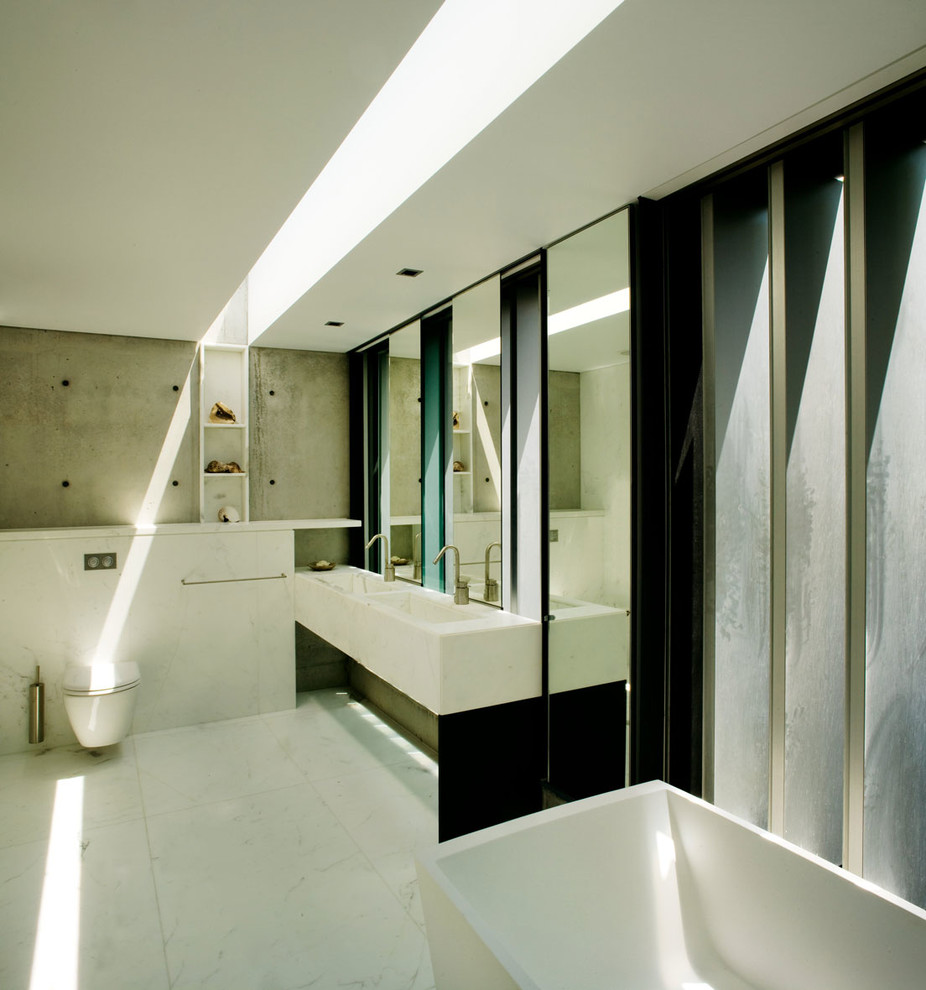 Inspiration for a large modern master bathroom in Sydney with an integrated sink, flat-panel cabinets, marble benchtops, a freestanding tub, a wall-mount toilet, white tile, stone tile and marble floors.