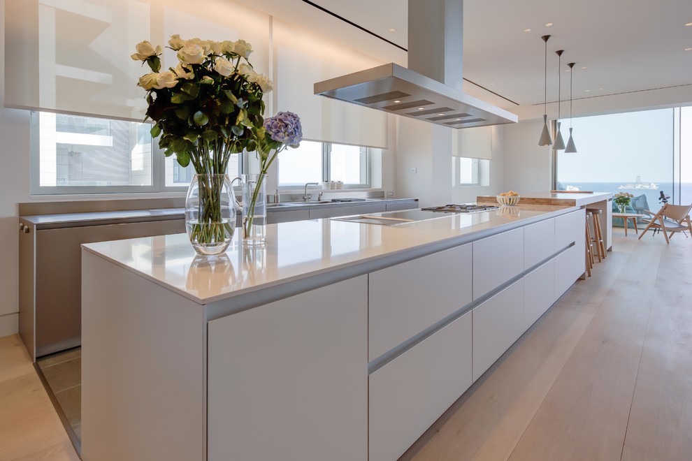 This is an example of a mid-sized beach style single-wall eat-in kitchen in Other with an integrated sink, flat-panel cabinets, beige cabinets, granite benchtops, beige splashback, terra-cotta splashback, panelled appliances, light hardwood floors, with island, beige floor and beige benchtop.