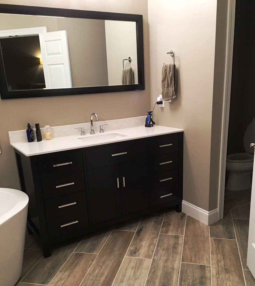 This is an example of a mid-sized contemporary master bathroom in Raleigh with flat-panel cabinets, dark wood cabinets, a freestanding tub, beige walls, ceramic floors, an undermount sink and engineered quartz benchtops.