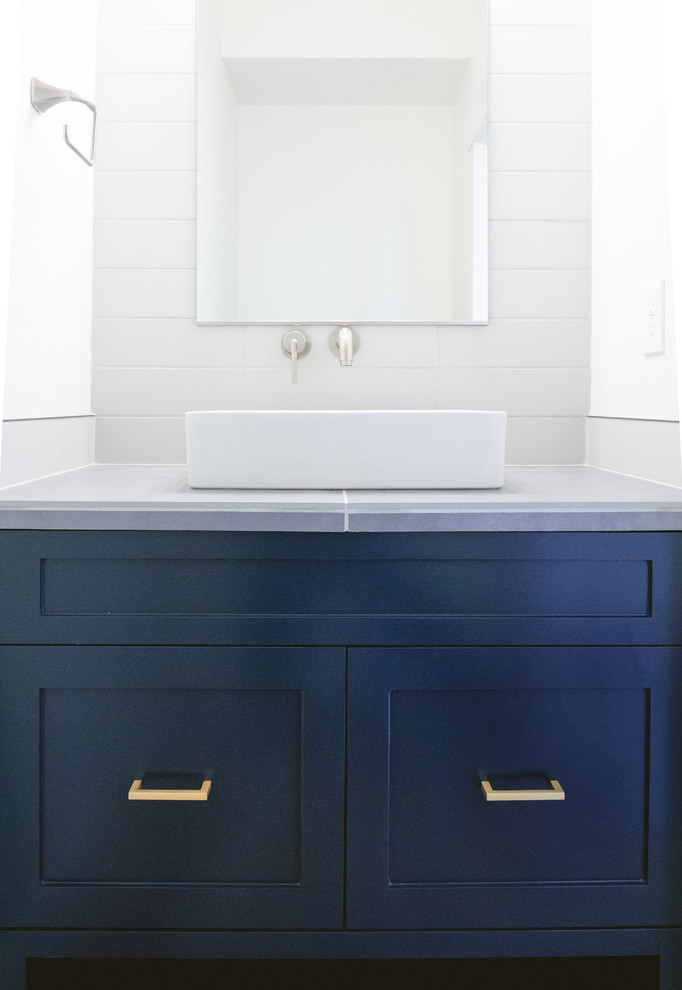 Small contemporary powder room in Portland with recessed-panel cabinets, blue cabinets, white tile, ceramic tile, white walls, a trough sink, solid surface benchtops and grey benchtops.