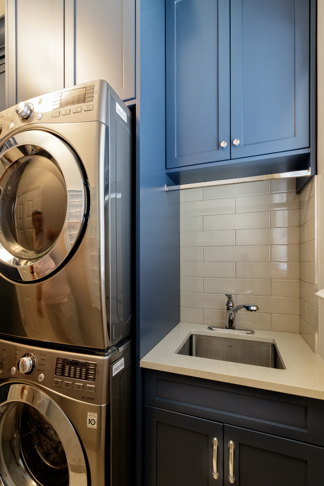 Design ideas for a mid-sized transitional single-wall dedicated laundry room in Vancouver with shaker cabinets, blue cabinets, quartzite benchtops, beige walls, porcelain floors, a stacked washer and dryer, beige floor and beige benchtop.