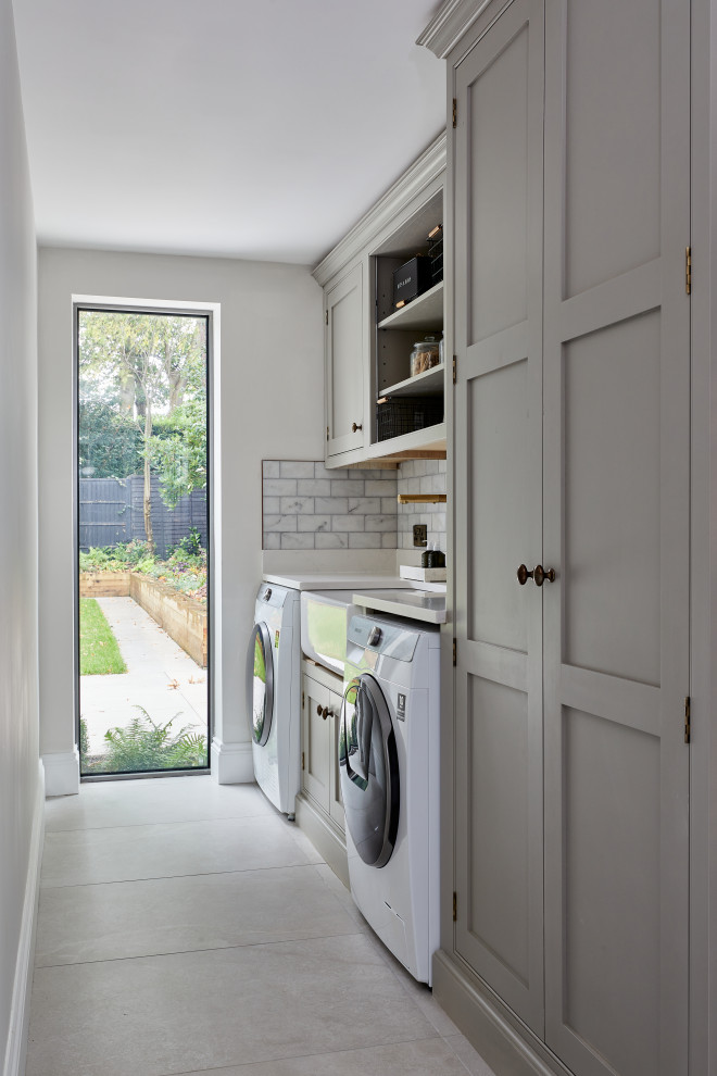 Inspiration for a mid-sized contemporary galley utility room in Wiltshire with shaker cabinets, grey cabinets, solid surface benchtops, white splashback, marble splashback, porcelain floors, an integrated washer and dryer and white benchtop.