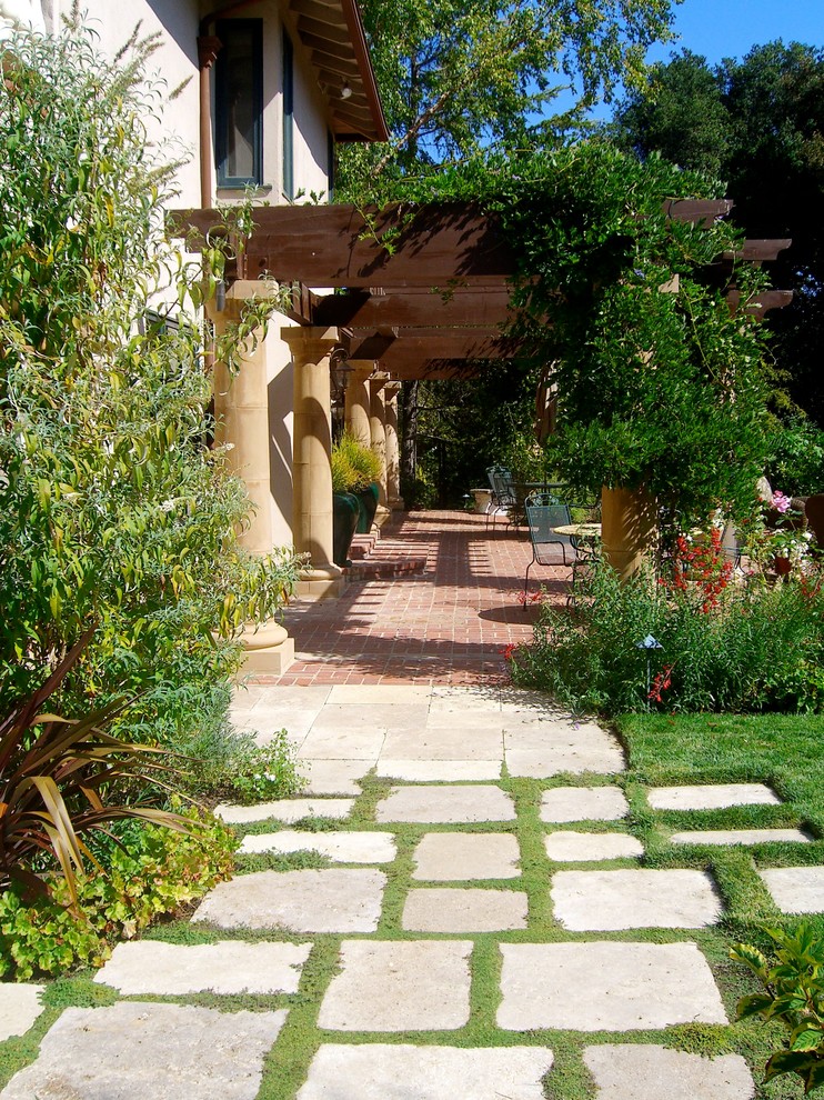This is an example of a mid-sized mediterranean backyard patio in San Francisco with natural stone pavers and a pergola.