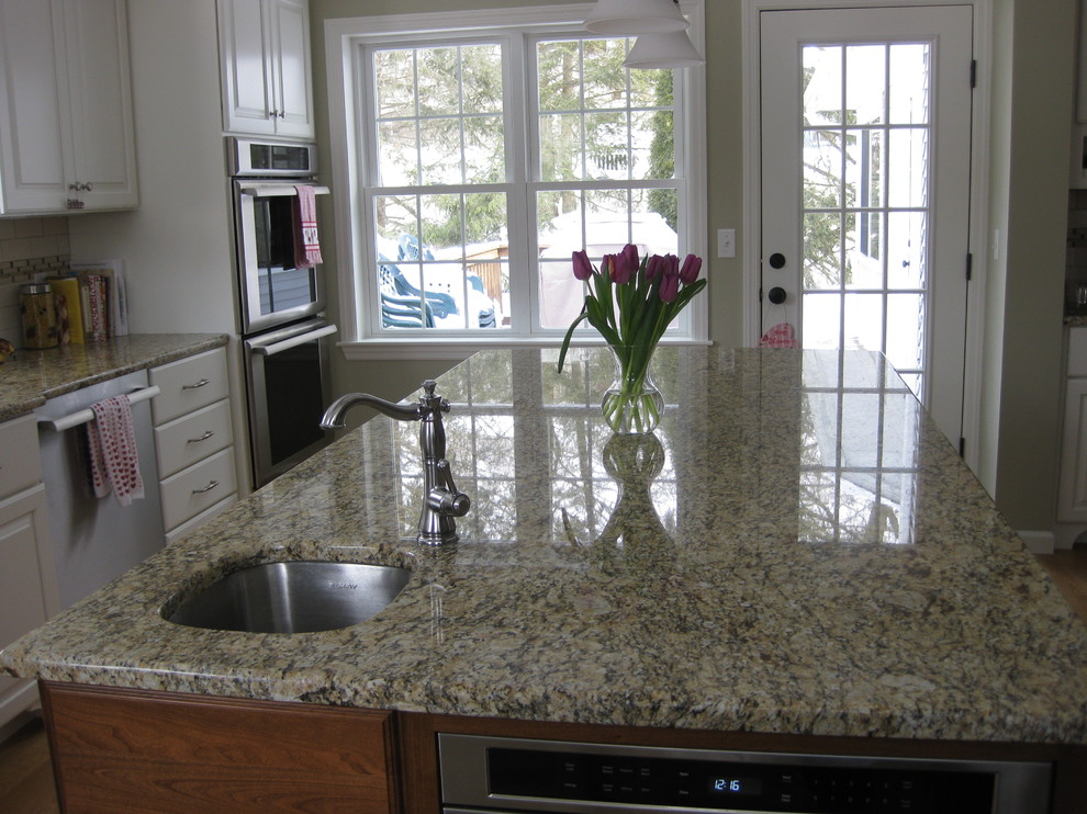 Transitional u-shaped medium tone wood floor eat-in kitchen photo in Boston with an undermount sink, raised-panel cabinets, white cabinets, granite countertops, white backsplash, ceramic backsplash, stainless steel appliances, an island and beige countertops