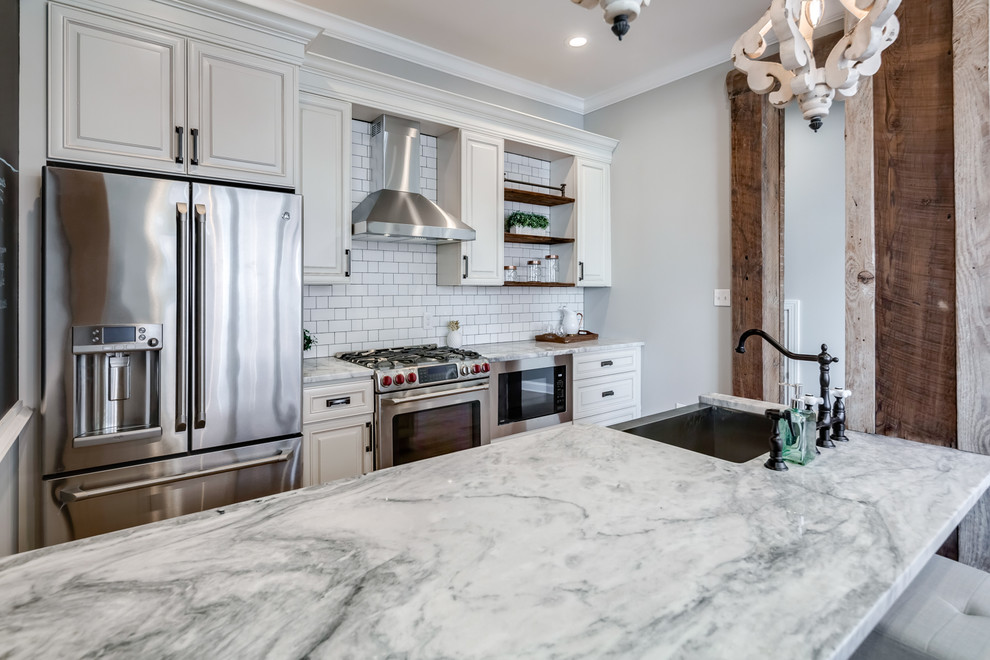 Mid-sized modern galley eat-in kitchen in Philadelphia with a farmhouse sink, raised-panel cabinets, beige cabinets, granite benchtops, white splashback, cement tile splashback, stainless steel appliances, light hardwood floors, no island and white benchtop.