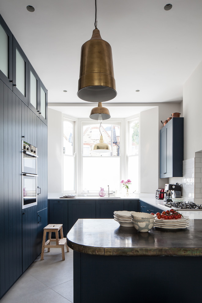 Inspiration for a transitional u-shaped separate kitchen in London with shaker cabinets, blue cabinets, white splashback, subway tile splashback, panelled appliances, a peninsula, grey floor and white benchtop.