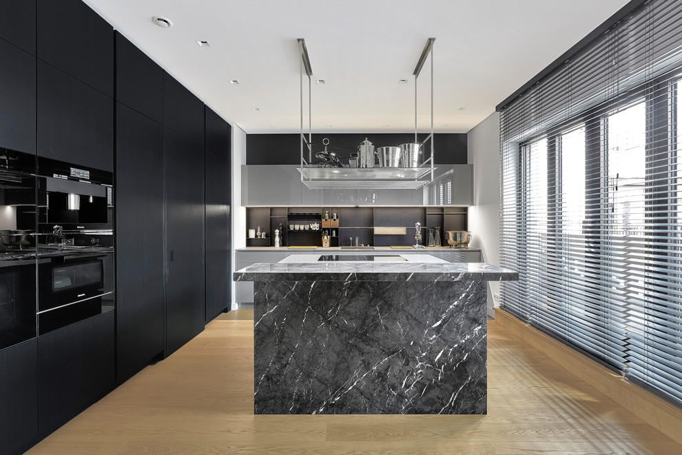 This is an example of a mid-sized contemporary l-shaped separate kitchen in Berlin with flat-panel cabinets, black cabinets, marble benchtops, black splashback, black appliances, light hardwood floors, with island, beige floor and black benchtop.