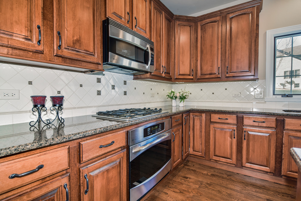 Eat-in kitchen - large transitional u-shaped medium tone wood floor eat-in kitchen idea in Chicago with a double-bowl sink, raised-panel cabinets, distressed cabinets, granite countertops, white backsplash, ceramic backsplash, stainless steel appliances and an island