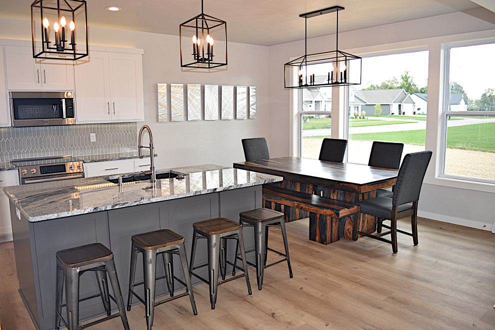 Inspiration for a large light wood floor eat-in kitchen remodel with an undermount sink, recessed-panel cabinets, white cabinets, granite countertops, gray backsplash, ceramic backsplash, stainless steel appliances, an island and multicolored countertops