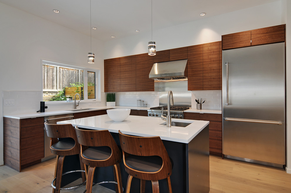 Design ideas for a large midcentury l-shaped kitchen in Seattle with an undermount sink, flat-panel cabinets, medium wood cabinets, quartz benchtops, white splashback, stainless steel appliances, with island, white benchtop, subway tile splashback and light hardwood floors.