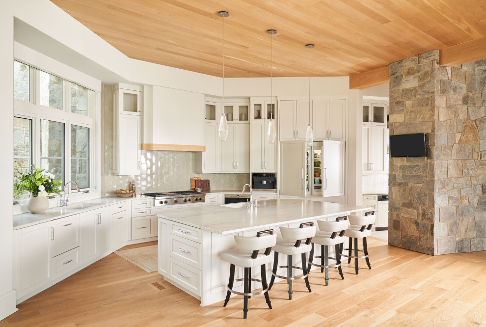 Design ideas for a transitional l-shaped open plan kitchen in Houston with an undermount sink, shaker cabinets, white cabinets, grey splashback, stainless steel appliances, light hardwood floors, with island, beige floor, white benchtop and wood.