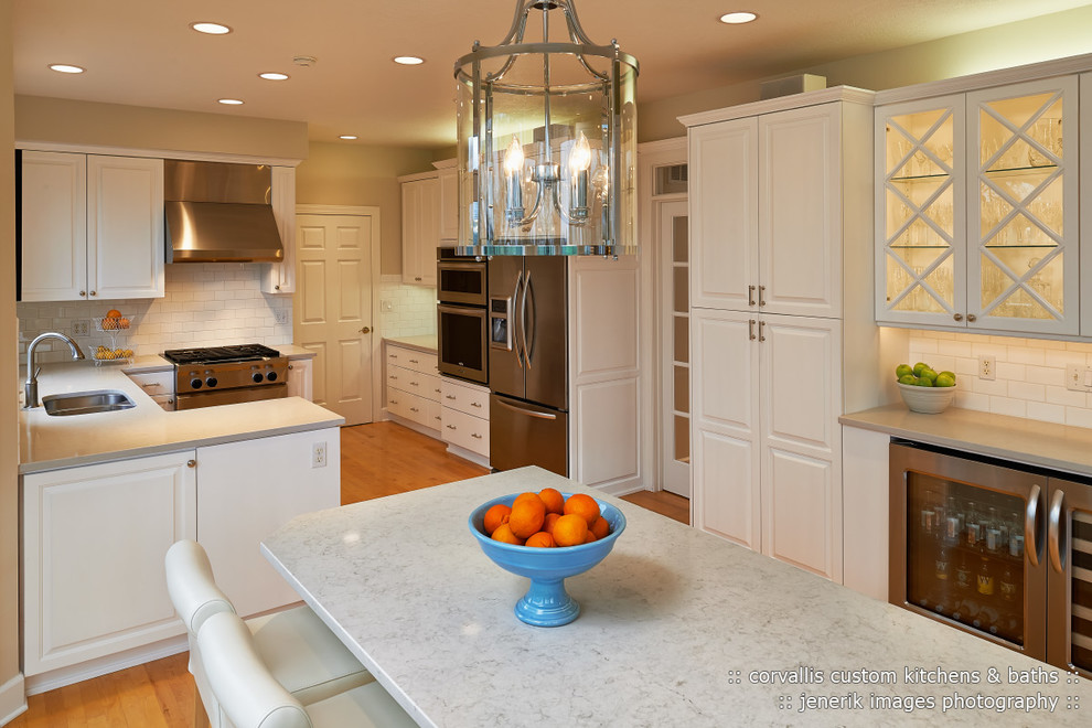 Transitional medium tone wood floor home design photo with an undermount sink, raised-panel cabinets, white cabinets, quartzite countertops, white backsplash, subway tile backsplash, stainless steel appliances and no island