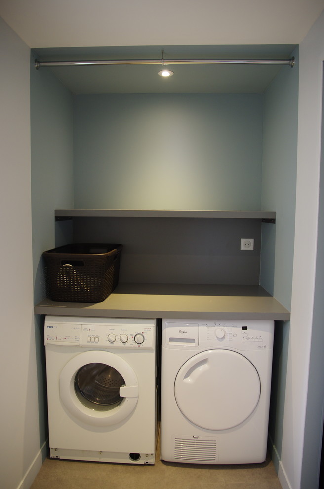 This is an example of a mid-sized contemporary single-wall utility room in Paris with laminate benchtops, blue walls, vinyl floors, a side-by-side washer and dryer, open cabinets, brown floor and beige benchtop.