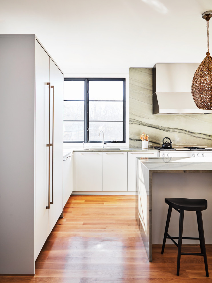 Inspiration for a modern u-shaped eat-in kitchen in New York with an undermount sink, flat-panel cabinets, white cabinets, grey splashback, panelled appliances, light hardwood floors, with island, grey benchtop and stone slab splashback.