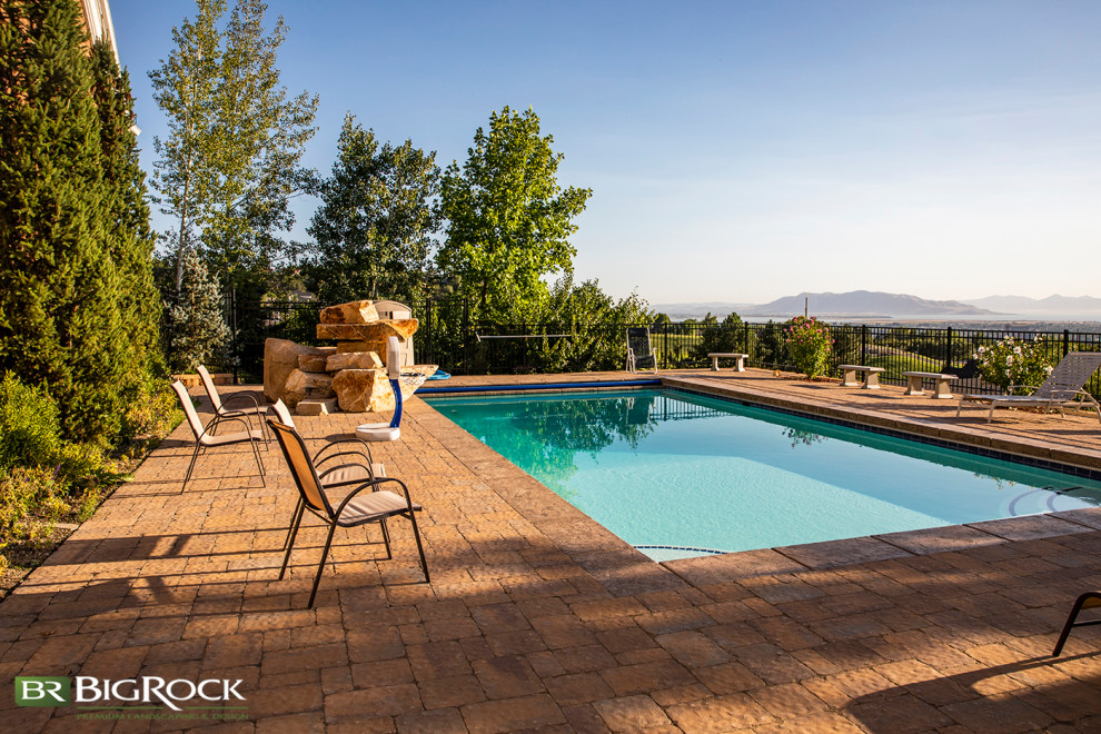 Imagen de piscina clásica grande rectangular en patio trasero con paisajismo de piscina y adoquines de ladrillo