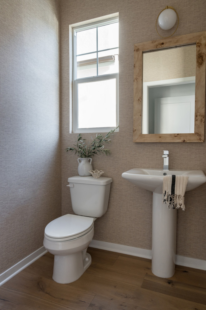 Inspiration for a small scandinavian cloakroom in Los Angeles with beige walls, light hardwood flooring, beige floors, a freestanding vanity unit, wallpapered walls, white cabinets and a pedestal sink.