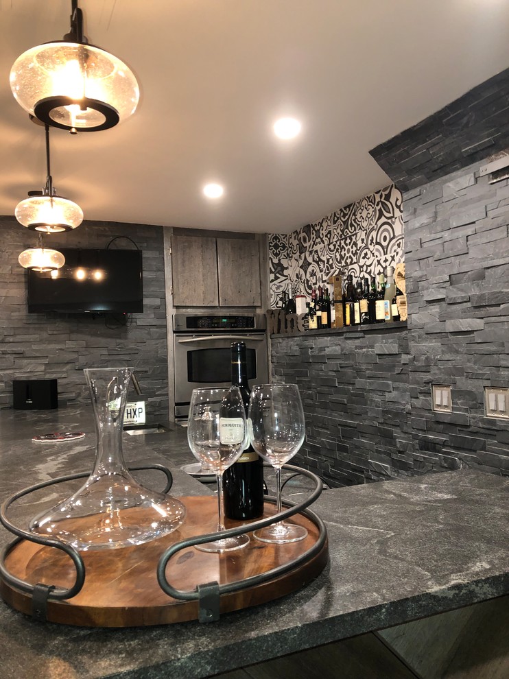 Inspiration for a mid-sized contemporary l-shaped seated home bar in New York with soapstone benchtops, grey splashback, slate splashback and black benchtop.