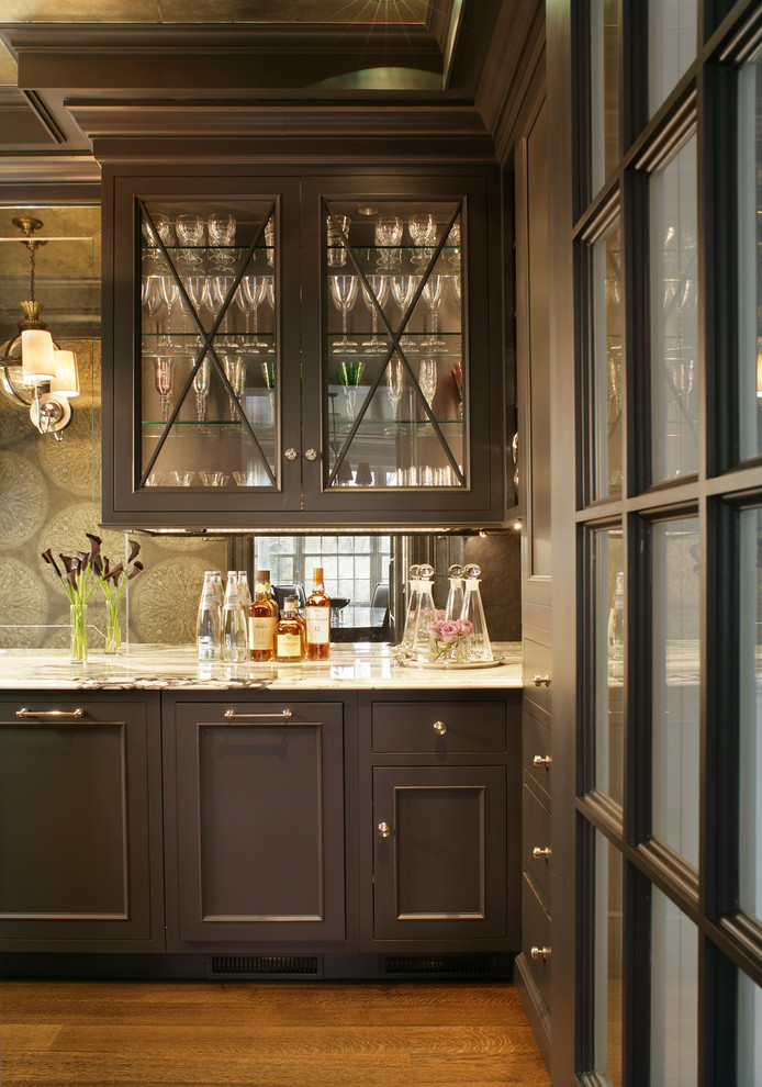 This is an example of a mid-sized transitional single-wall wet bar in New York with an undermount sink, glass-front cabinets, brown cabinets, marble benchtops, dark hardwood floors, brown floor and mirror splashback.
